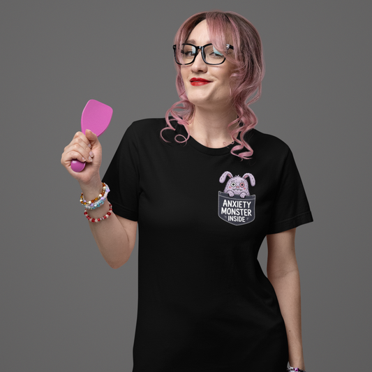 Person wearing a black t-shirt with a graphic design that says Anxiety Monster Inside, holding a pink spatula against a gray background