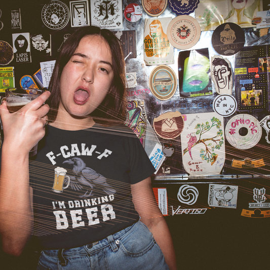 Person wearing a t-shirt with a graphic design F-CAW-F I'm Drinking Beer in front of a wall covered in stickers.