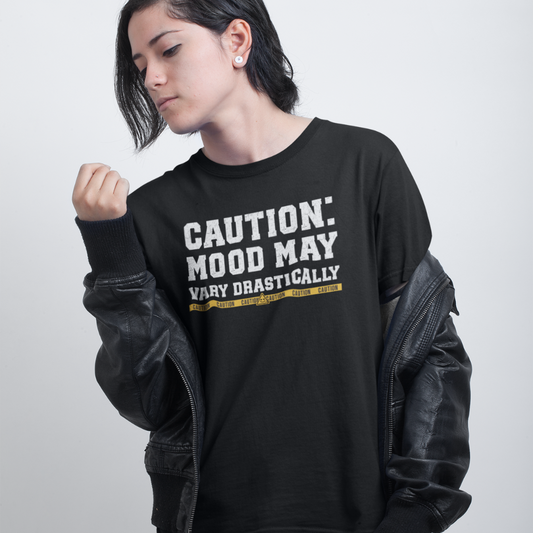 Person wearing a black sweatshirt with text 'CAUTION: MOOD MAY VARY DRAMATICALLY' on a plain background