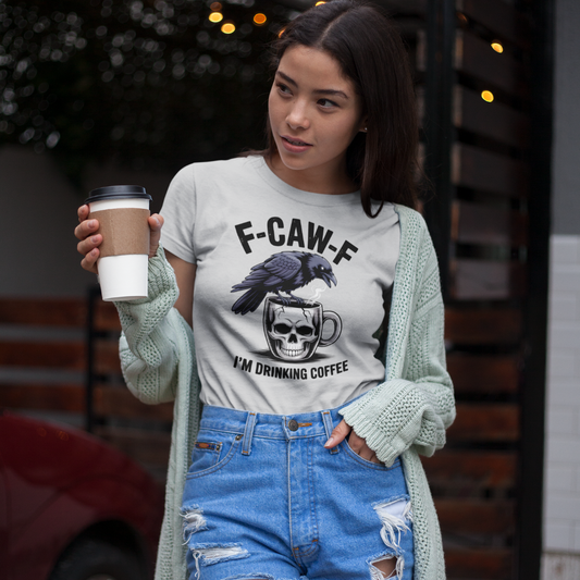 Woman wearing a graphic t-shirt with F-Caw-C I'm Drinking Coffee  and Crow on a skull coffee mug illustration, women is holding a coffee cup.